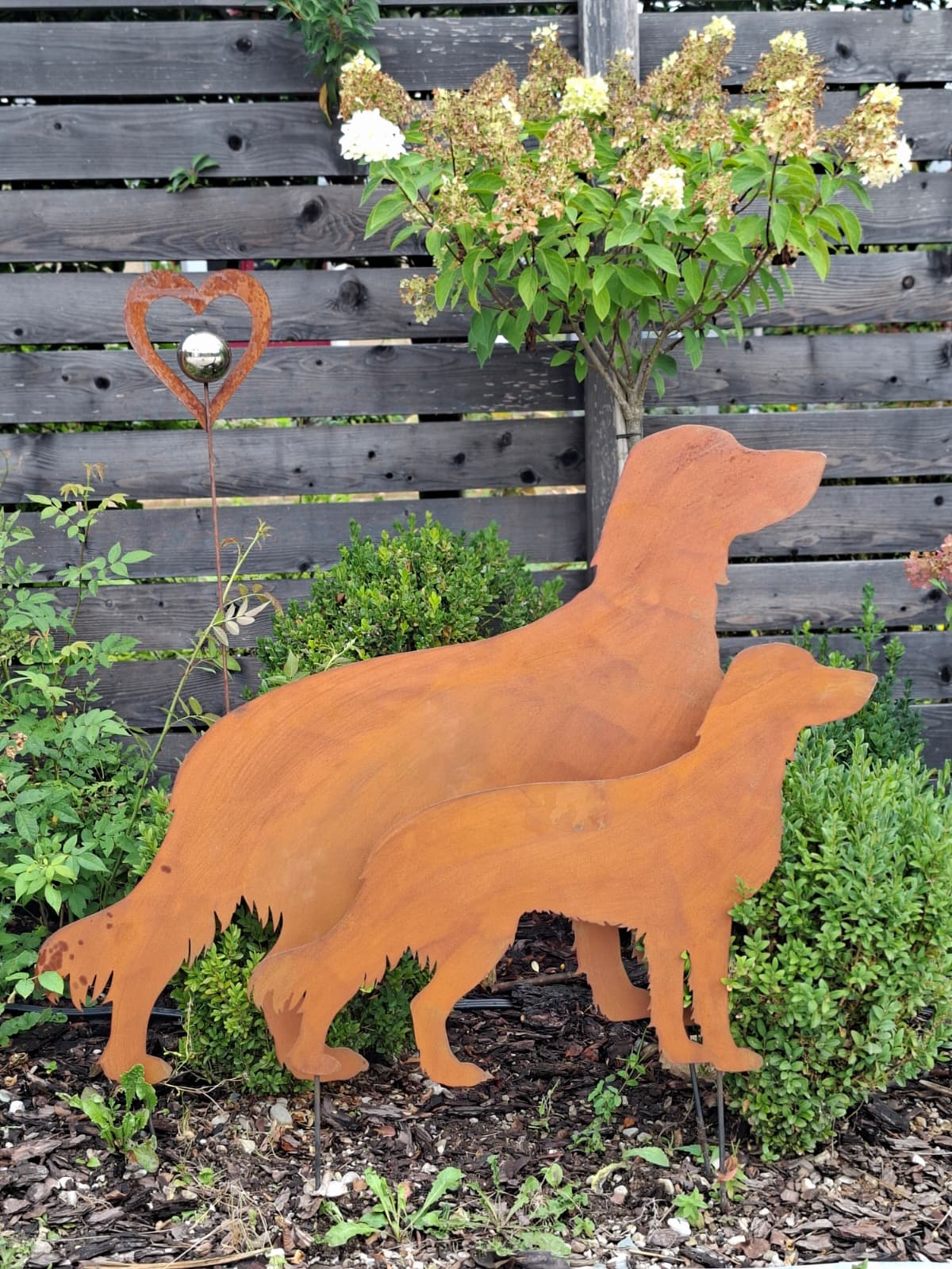 Zwei Gartenfiguren als Jagdhund-Silhouette in Rostoptik, groß und klein, im Garten