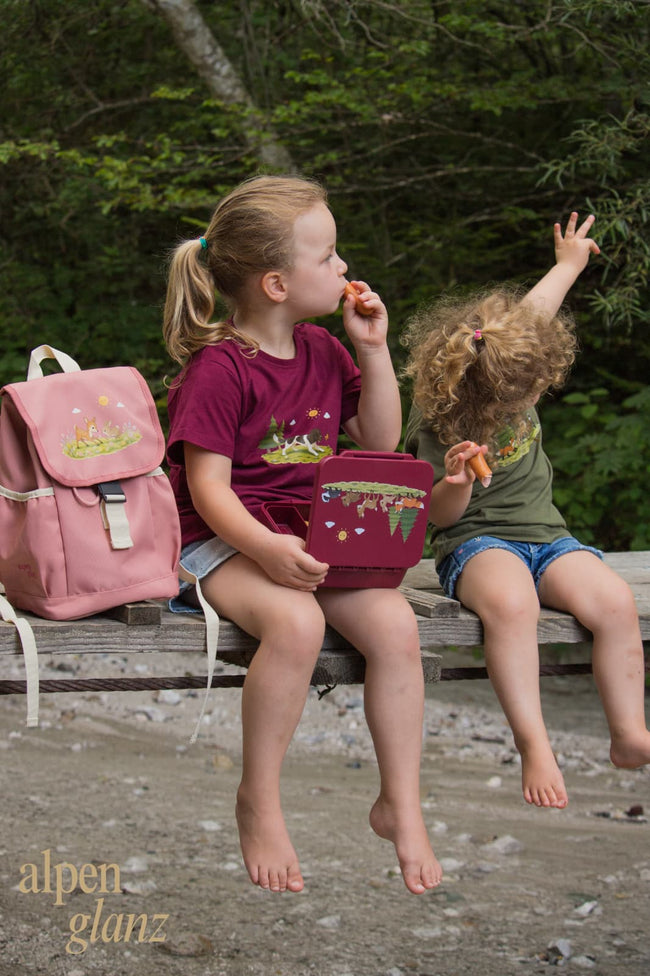 Zwei Kinder im Wald mit Alpenglanz-Waldtier-Shirts, rosa Rucksack und Lunchbox