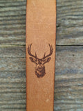 Brauner Leder-Schlüsselanhänger mit graviertem Hirschkopf auf einem Holztisch